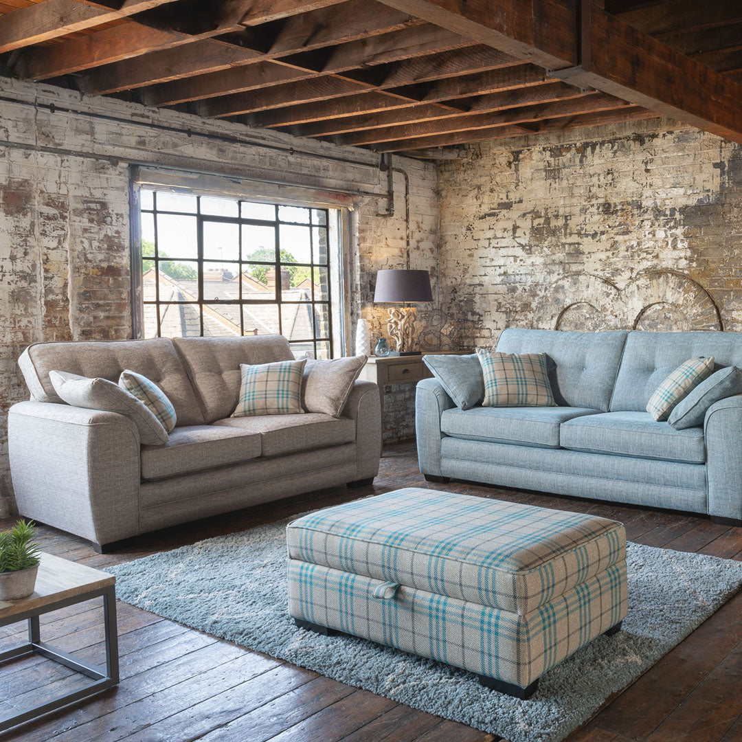An image of two neutral colour sofas and a blue ottoman positioned between them. The ottoman is sat on a fluffy grey rug.