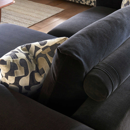 Dark gray sofa with a patterned pillow on a wooden floor.