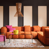 An image of a large corner sofa in bright orange andbright pink cushions. The sofa has a cube design and can be built in modular pieces. 
