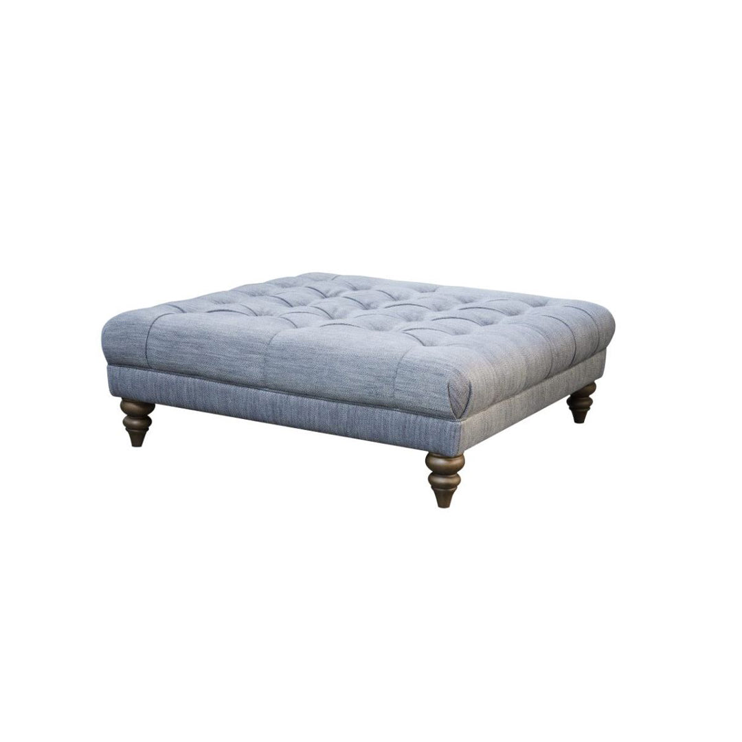 An image of the emma footstool on a white background. The stool is in  a light Grey/ Blue Fabric with dark wood legs. 