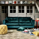 A lifestyle image of the Alexander and James Saddler Armchair. The sofa is in a green velvet Fabric and has magazines laid on the floor in front of it. 